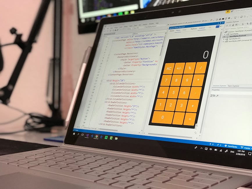 Close-up view of a laptop on a desk displaying a software development environment with lines of code on the screen, alongside a large orange calculator interface with white buttons for numerical calcu